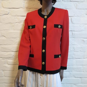 May include: A bright red blazer featuring a black trim along the round neckline, front placket, cuffs, and two faux chest pockets. The jacket is secured with five gold-toned circular buttons down the center front, with additional gold buttons on the pockets.
