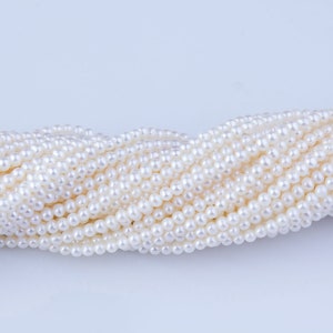May include: A strand of white freshwater pearls, arranged in a wavy pattern. The pearls are smooth and lustrous, and they are all approximately the same size.