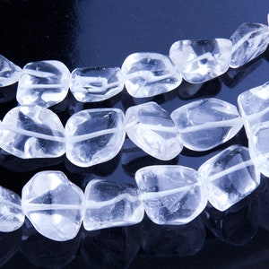 Pode incluir: Um fio de contas de cristal de quartzo transparente, cada conta &eacute; facetada e tem um formato ligeiramente irregular. As contas s&atilde;o enfiadas em um fio transparente e est&atilde;o dispostas em um padr&atilde;o solto e fluido.