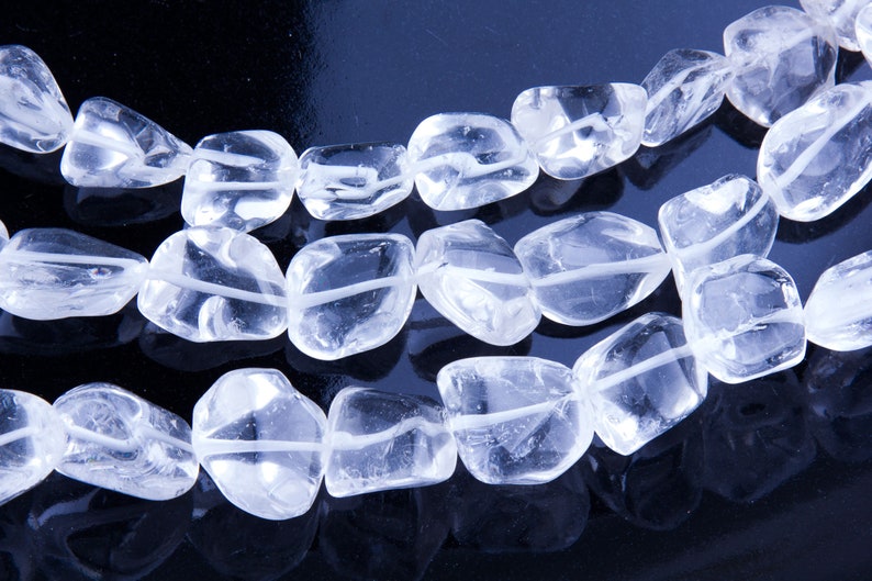 Pode incluir: Um fio de contas de cristal de quartzo transparente, cada conta &eacute; facetada e tem um formato ligeiramente irregular. As contas s&atilde;o enfiadas em um fio transparente e est&atilde;o dispostas em um padr&atilde;o solto e fluido.