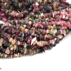 May include: A strand of multi-colored tourmaline gemstone chips. The chips are a mix of pink, green, black, and brown.