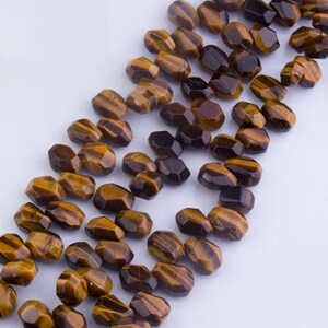 May include: A strand of faceted tiger's eye beads in shades of brown and gold. The beads are all approximately the same size and shape, and they are strung together on a clear thread.