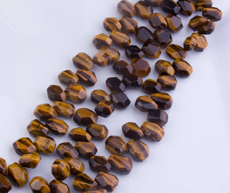 May include: A strand of faceted tiger's eye beads in shades of brown and gold. The beads are all approximately the same size and shape, and they are strung together on a clear thread.