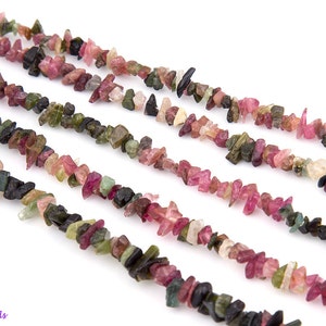 May include: A strand of multi-colored gemstone chips, including pink, green, and black, arranged in a row. The chips are irregular in shape and size, and they are strung together on a clear thread.