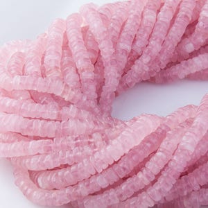May include: A strand of pink rose quartz beads, each bead is faceted and has a slightly irregular shape. The beads are strung together to form a long necklace.