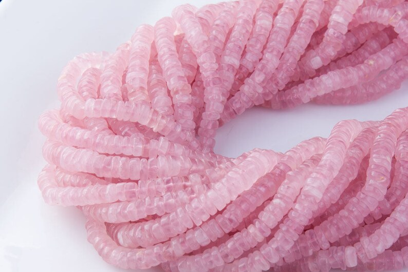 May include: A strand of pink rose quartz beads, each bead is faceted and has a slightly irregular shape. The beads are strung together to form a long necklace.