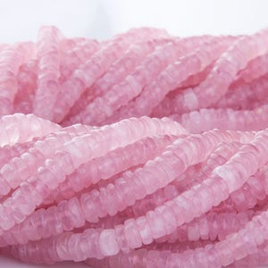 May include: A strand of pink rose quartz beads. The beads are faceted and have a slightly irregular shape. They are strung on a clear thread.
