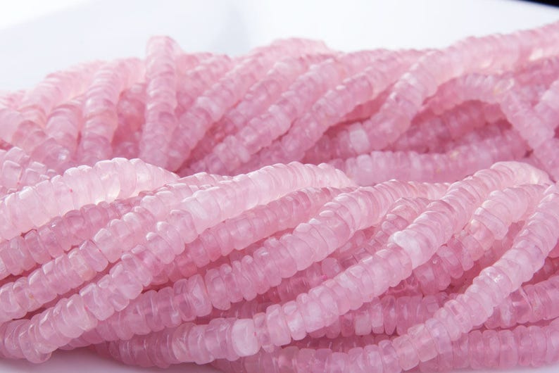May include: A strand of pink rose quartz beads. The beads are faceted and have a slightly irregular shape. They are strung on a clear thread.