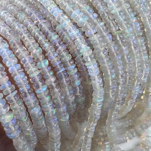 May include: Multiple strands of small, translucent, disc-shaped opal beads. Each bead features a smooth, rounded edge and displays a subtle, iridescent play of color with flashes of blue, green, and pink against a milky, semi-transparent base.