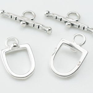 May include: Silver toggle clasp with a rectangular shape and a round loop. The clasp is designed to be used with a necklace or bracelet.