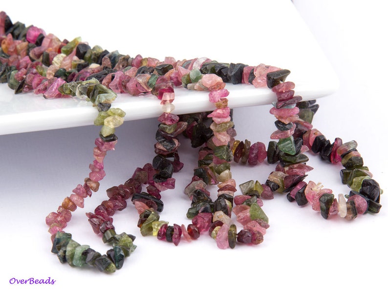 May include: A strand of multi-colored, chip-shaped, natural gemstone beads. The beads are pink, green, and black. The beads are strung on a clear thread.