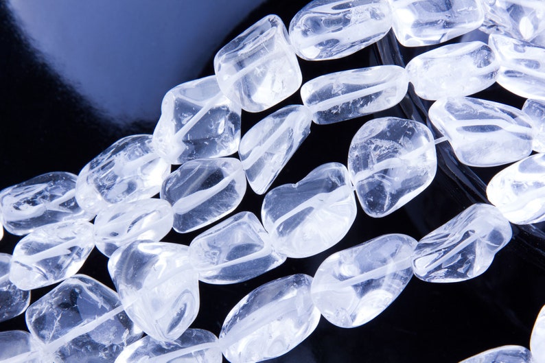 Pode incluir: Um fio de contas de cristal de quartzo transparente, cada conta &eacute; facetada e tem um acabamento liso e polido. As contas s&atilde;o dispostas em um padr&atilde;o solto e fluido, criando uma sensa&ccedil;&atilde;o de movimento e energia.