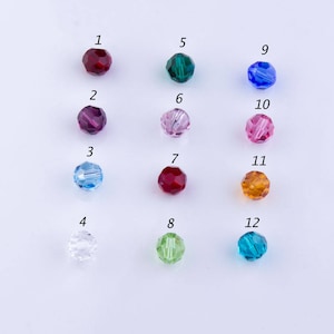 May include: Twelve round glass beads in various colors, numbered 1 through 12. The beads are arranged in four rows of three beads each.