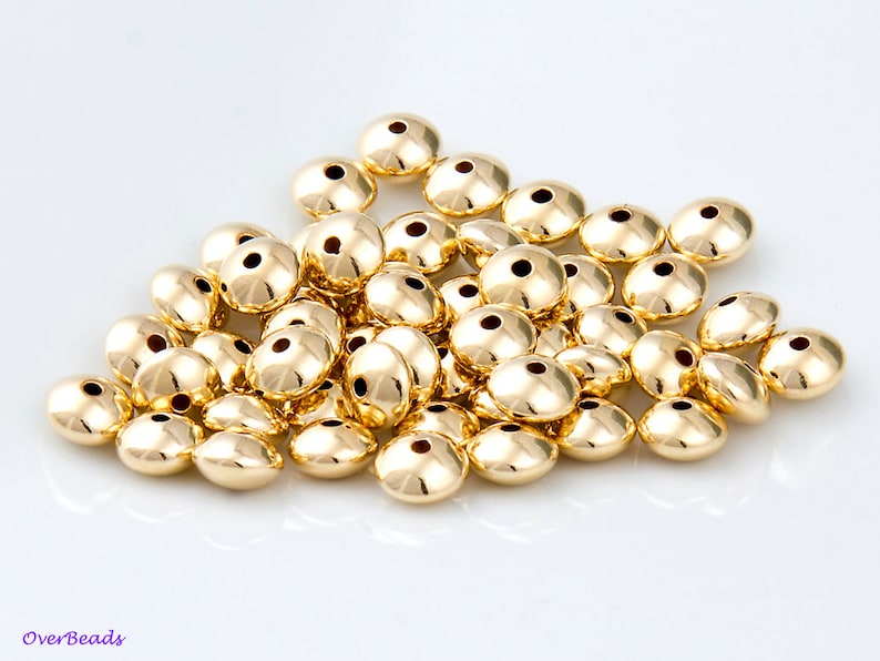 May include: A pile of gold-colored metal beads. The beads are round and have a smooth, shiny finish. They are about 1/2 inch in diameter.