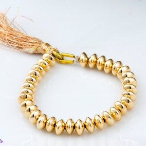 May include: A gold bracelet with a tassel made of brown and beige fibers. The bracelet is made of round, gold beads.
