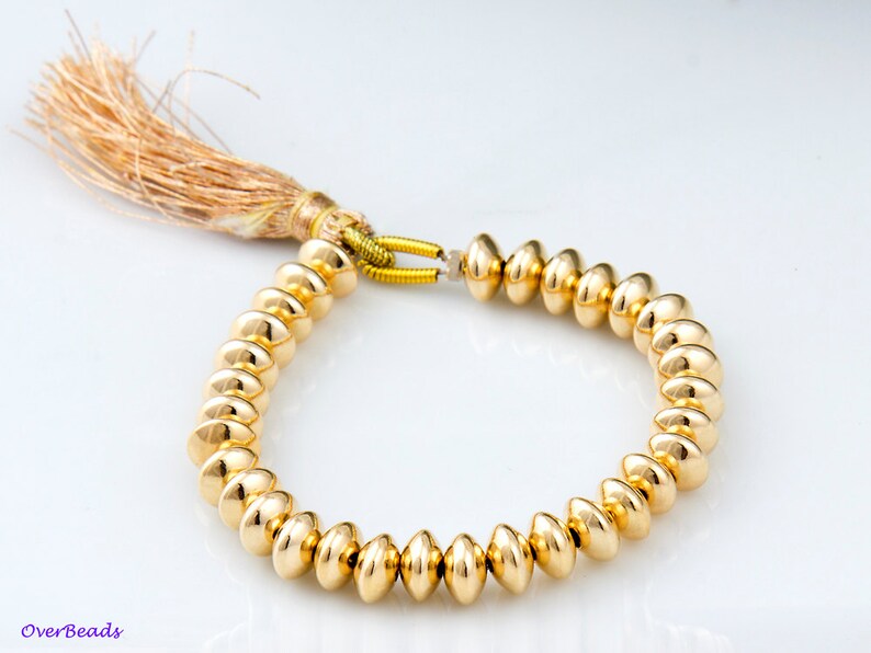 May include: A gold bracelet with a tassel made of brown and beige fibers. The bracelet is made of round, gold beads.