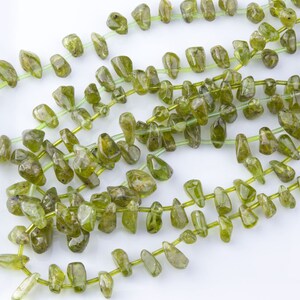 Puede incluir: Una hebra de cuentas de piedras preciosas verdes, cada cuenta tiene una forma irregular y tosca. Las cuentas est&aacute;n enhebradas en un hilo transparente.