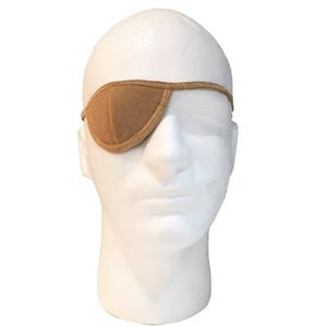 May include: A tan eye patch is displayed on a white mannequin head. The eye patch is made of a soft material and is designed to cover one eye. The eye patch is held in place by a thin strap that goes around the head. The eye patch is a solid tan color.