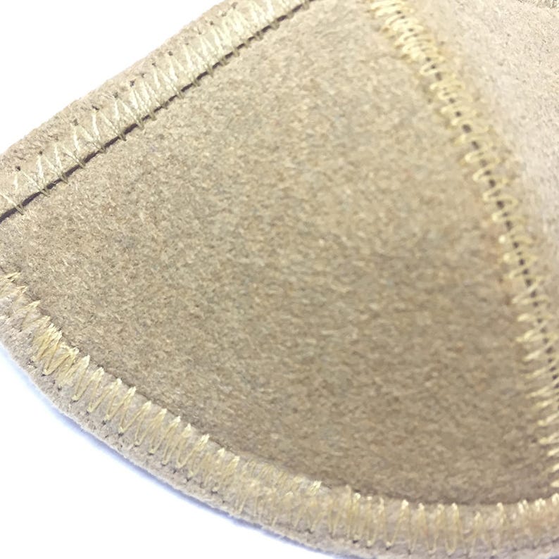 May include: Close-up of a beige, semi-circular fabric pad with a textured surface. The edges are outlined with a lighter beige stitching, creating a defined border. The pad appears to be made of a soft, possibly felt-like material.