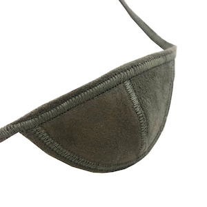 May include: A dark olive green eye patch with a stitched border and a strap. The eye patch is made of a soft, suede-like material. The strap is thin and appears to be made of the same material as the eye patch.