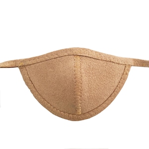 May include: A tan eye patch with a curved shape and a textured surface. The edges are stitched with a contrasting thread, and it has thin straps extending from each side.
