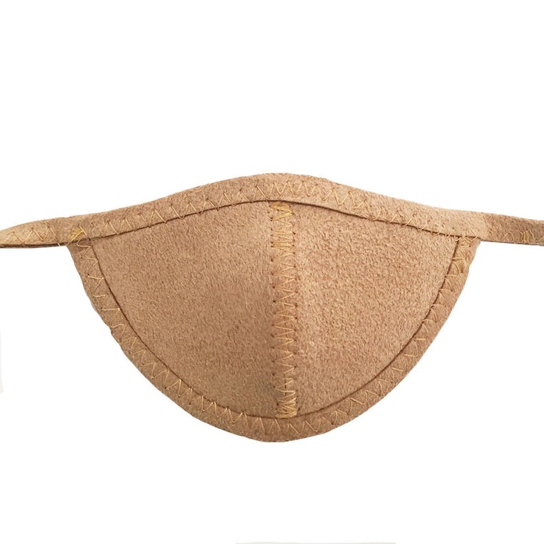 May include: A tan eye patch with a curved shape and a textured surface. The edges are stitched with a contrasting thread, and it has thin straps extending from each side.