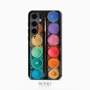 May include: A rectangular phone case featuring a printed design of a watercolor paint set with twelve circular pans of various colors arranged in two columns, separated by a thin paintbrush placed vertically in the center of the case.