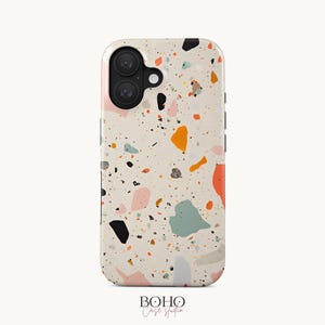 May include: A mobile phone case featuring a cream-colored background with a multi-colored terrazzo pattern consisting of scattered shapes in shades of orange, black, light blue, pink, and grey. The case has a black camera lens cutout area.