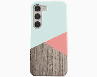May include: A smartphone case featuring a geometric design with a light mint green top section, a coral pink triangular accent, and a bottom section with a realistic brown wood grain texture. The case includes cutouts for a triple camera system.