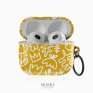 Op de afbeelding: Een gele Airpods-hoes met een wit abstract ontwerp. De hoes heeft een witte band met een metalen ring.