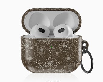Puede incluir: Estuche AirPods marrón abierto con motivos florales y auriculares blancos en el interior. El estuche presenta un patrón floral blanco y un anillo negro para sujetar. El texto "BOHO Case studio" está en la parte inferior.