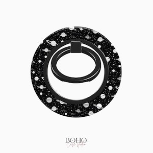 May include: Black phone ring holder with a white galaxy print. The ring is made of metal and has a textured finish.