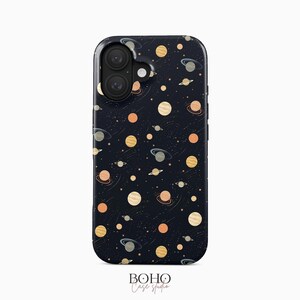 May include: A dark navy blue phone case featuring a repeating pattern of various planets, rings, and small stars in shades of peach, cream, and light gray. The design includes a camera cutout at the top left corner and the text Boho Case Studio below.