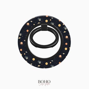May include: A black phone ring holder with a galaxy print. The print features small planets, stars, and dots in shades of orange, yellow, and white on a dark blue background.