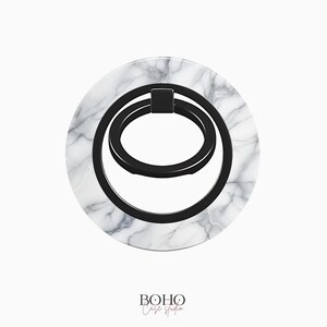 May include: A white marble phone ring holder with a black metal ring. The ring is designed to be used as a stand or grip for a phone.