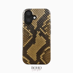 Könnte beinhalten: Eine rechteckige Smartphone-Hülle mit einem realistischen Schlangenhautmuster in Braun und Beige. Die Hülle hat oben links eine schwarze Kameraaussparung mit zwei runden Linsen und einem Blitzlicht. Darunter befindet sich der Text Boho Case Studio.