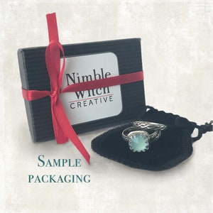 A sample of a ring set in Etsy packaging from the Nimble Witch Creative shop featuring a ring sized gift box and a black velvet pouch.