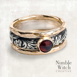 May include: A silver and gold ring with a red gemstone set in the center. The ring is decorated with a floral design.