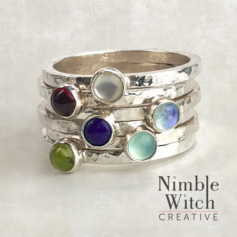 Shown on model's hand is a stacking set of 6 rings with 4mm natural birthstones. Rings are made of hammered,14 gauge, square, sterling silver. In this set is a Garnet, Mother of Pearl, Peridot, Lapis, Moonstone, and Aqua Calcedony.