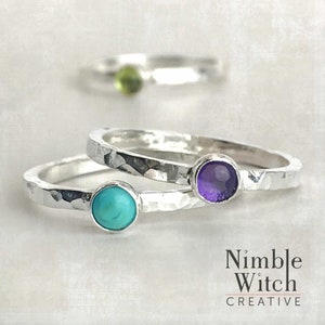 Three stacking natural birthstone rings. Each ring is set with a single stone in fine silver. Birthstones here are a Turquoise, Amethyst, and a Peridot which is shown in the background.