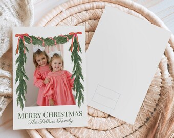 May include: Christmas card featuring a photo of two young girls in pink dresses, framed by a watercolor garland with red bows and berries. The card reads "MERRY CHRISTMAS The Sellars Family."