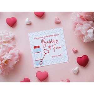 May include: A Valentine's Day card with a bubble-themed design, featuring a bubble wand and bottle illustration. The card reads "Bubbles of Fun!" and is surrounded by heart-shaped decorations and pink flowers on a pink background.