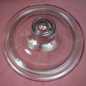Könnte beinhalten: Ein klarer Glaskuchenständer mit erhöhtem Zentrum und glatter, polierter Oberfläche. Der Ständer hat ein schlichtes, elegantes Design und ist perfekt zum Präsentieren von Kuchen, Torten oder anderen Desserts.