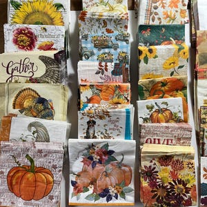 May include: A collection of decorative paper napkins with fall and harvest themes. Designs include pumpkins, sunflowers, trucks, and autumn leaves. Some napkins have text like "Gather" and "diggin' the season."