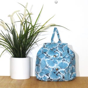 May include: A small blue backpack with a floral pattern. The backpack has a drawstring closure and a flap with a buckle.