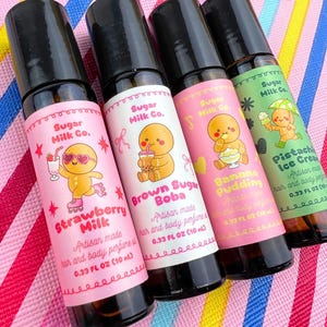 Peut inclure: Quatre flacons de parfum artisanaux avec des bouchons noirs et des étiquettes colorées. Les étiquettes présentent des personnages de dessins animés et les parfums : Strawberry Milk, Brown Sugar Boba, Banana Pudding et Pistachio Ice Cream. Chaque flacon contient 10 ml.