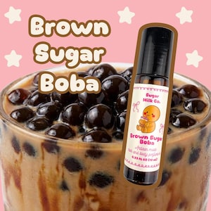 May include: A brown glass bottle of "Brown Sugar Boba" perfume sits in front of a glass of boba tea. The bottle has a black cap and a label with a cartoon character and the text "Sugar Milk Co.". The background is pink with white stars.