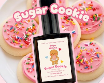 Könnte beinhalten: Eine schwarze Flasche "Sugar Cookie" Haar- und Körperparfümöl, 50 ml, mit einem Etikett mit einem Lebkuchenmann, der einen Kuchen hält. Die Flasche ist von glasierten Zuckerkeksen mit Streuseln umgeben.