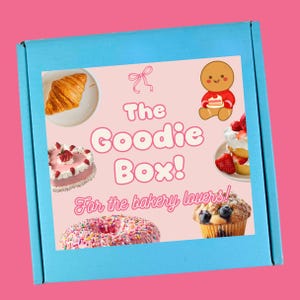 May include: A light blue box with a pink graphic that reads "The Goodie Box! For the bakery lovers!" The graphic includes illustrations of a croissant, cake, donut, muffin, and a gingerbread man.