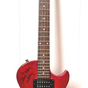 Puede incluir: Una guitarra eléctrica Epiphone Special roja y naranja con firmas. La guitarra tiene un clavijero negro con el logotipo de Epiphone y clavijas cromadas. El cuerpo es un degradado de rojo a naranja.